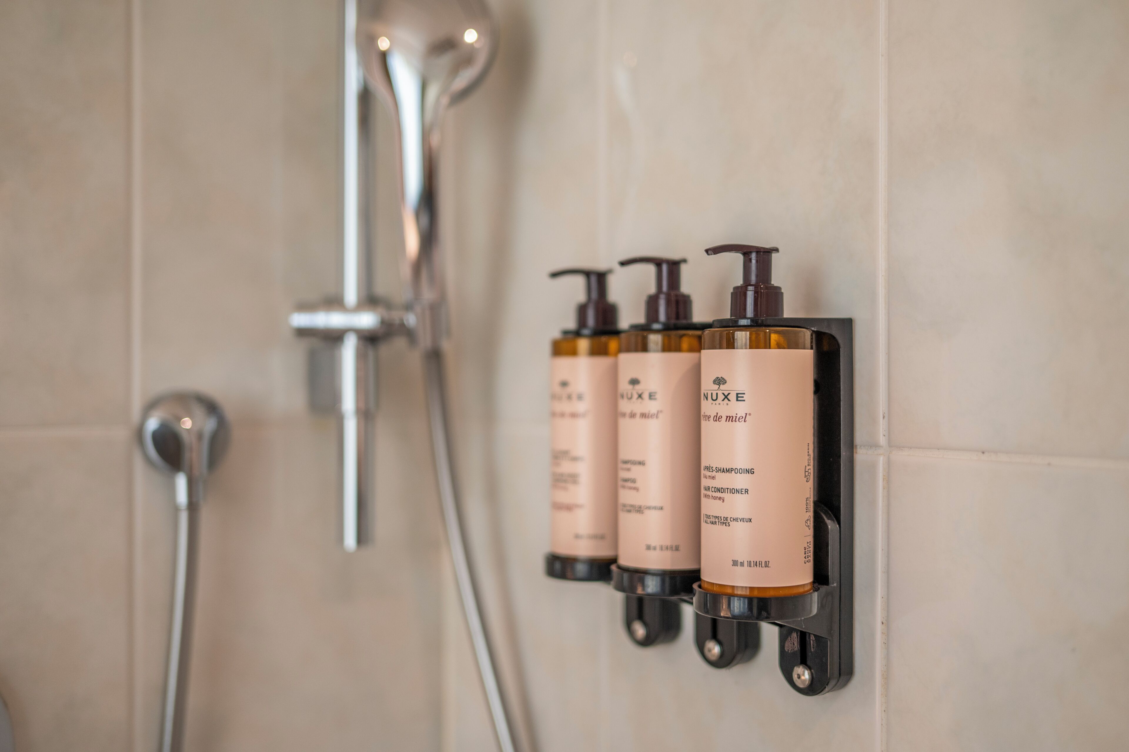 A bathroom with a wall-mounted shampoo dispenser and a shower head.