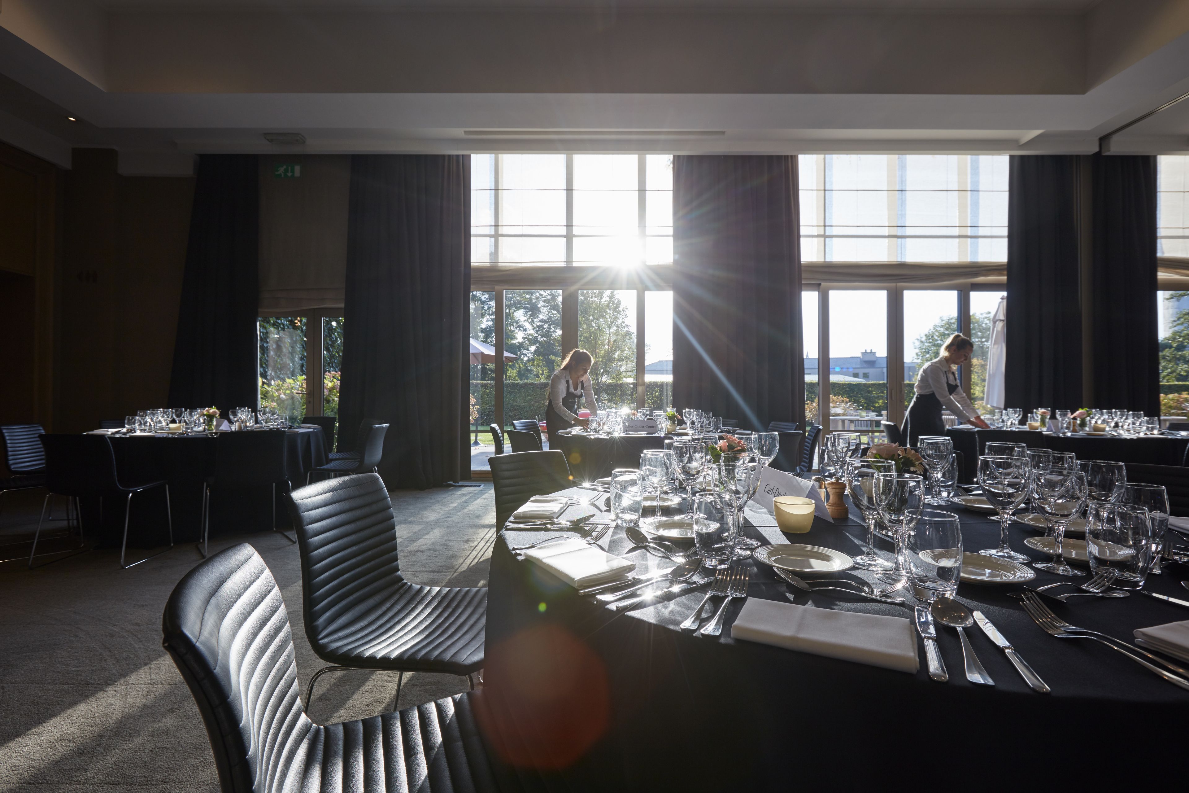 Un comedor bien iluminado con mesas dispuestas para una comida, ventanas amplias con luz natural y vistas al exterior.