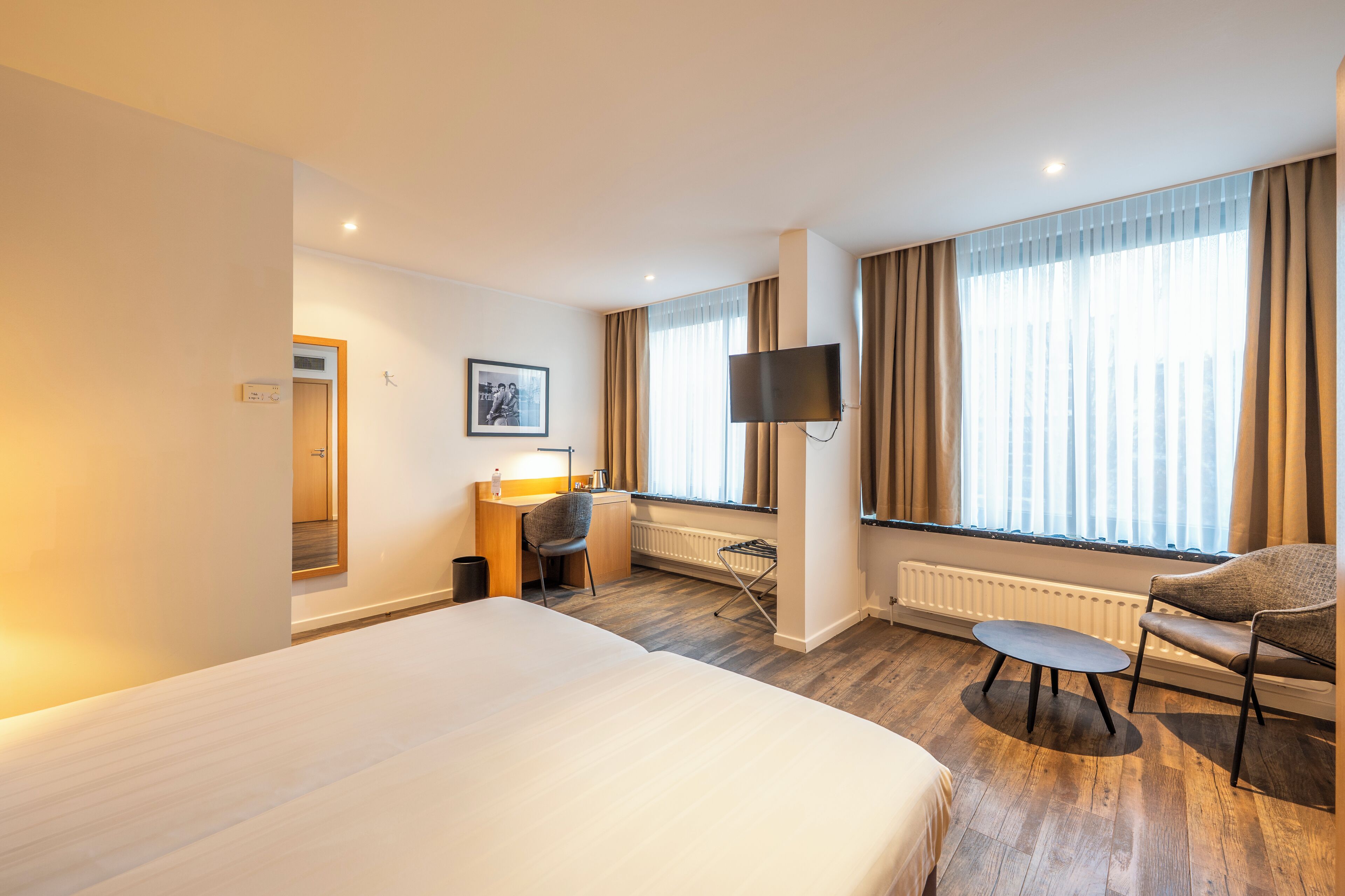 A hotel room with a large bed, a desk with a chair, a TV, and a window with curtains.