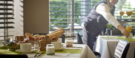 Un desayuno servido en una mesa para dos personas, con pan, bollería y bebidas.