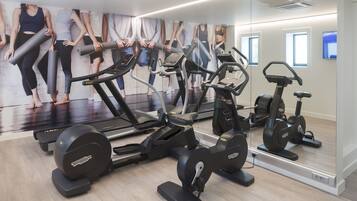 Un gimnasio con diversas máquinas de ejercicio, un espejo grande y una pared con imágenes de personas ejercitándose.
