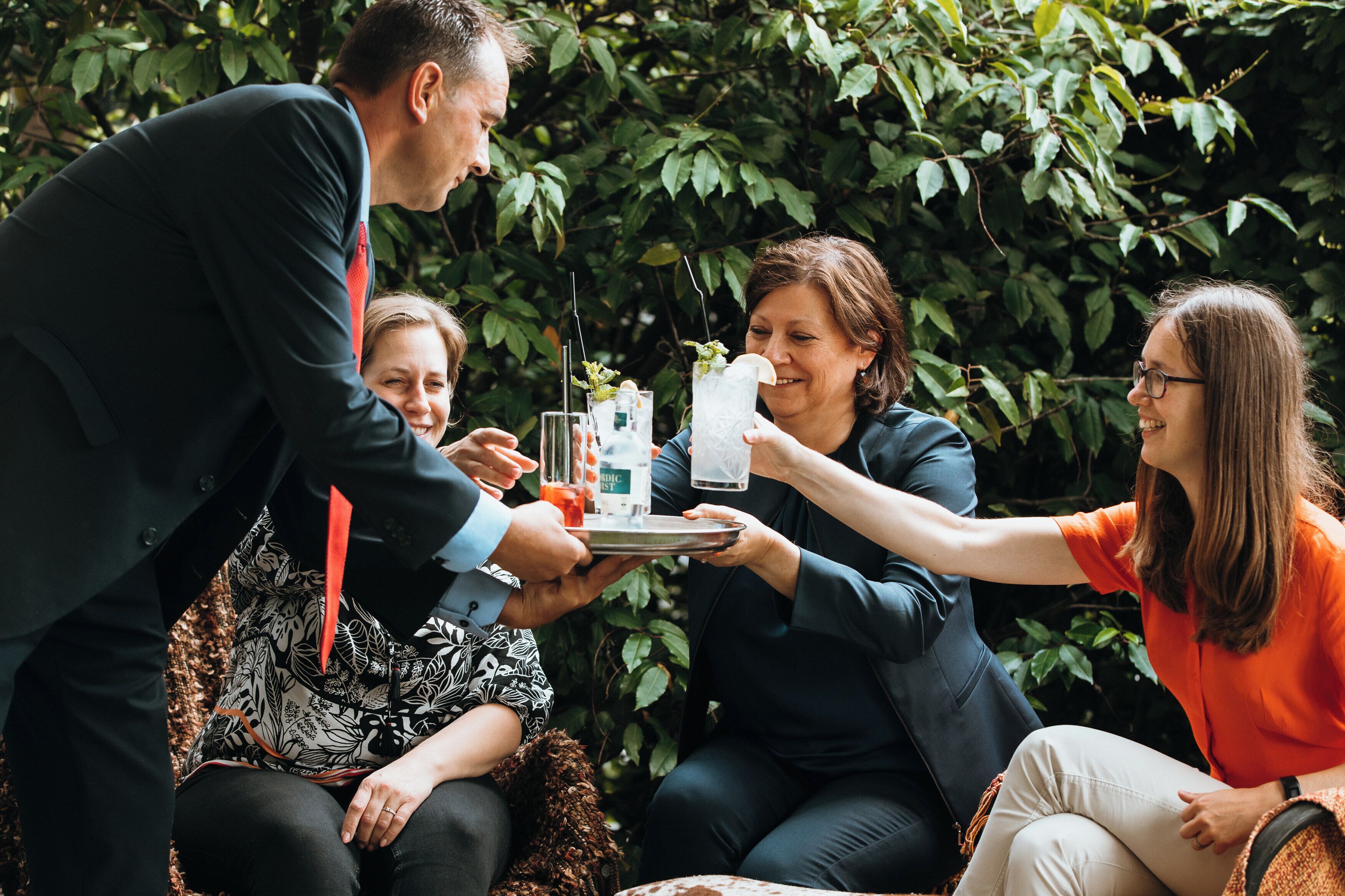 A group of people seated outdoors, engaged in conversation, with a tray of drinks and snacks.