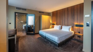 Une chambre d’hôtel moderne dotée d’un grand lit, d’une armoire intégrée, d’un petit coin salon et d’une salle de bain avec un mur recouvert de carreaux.