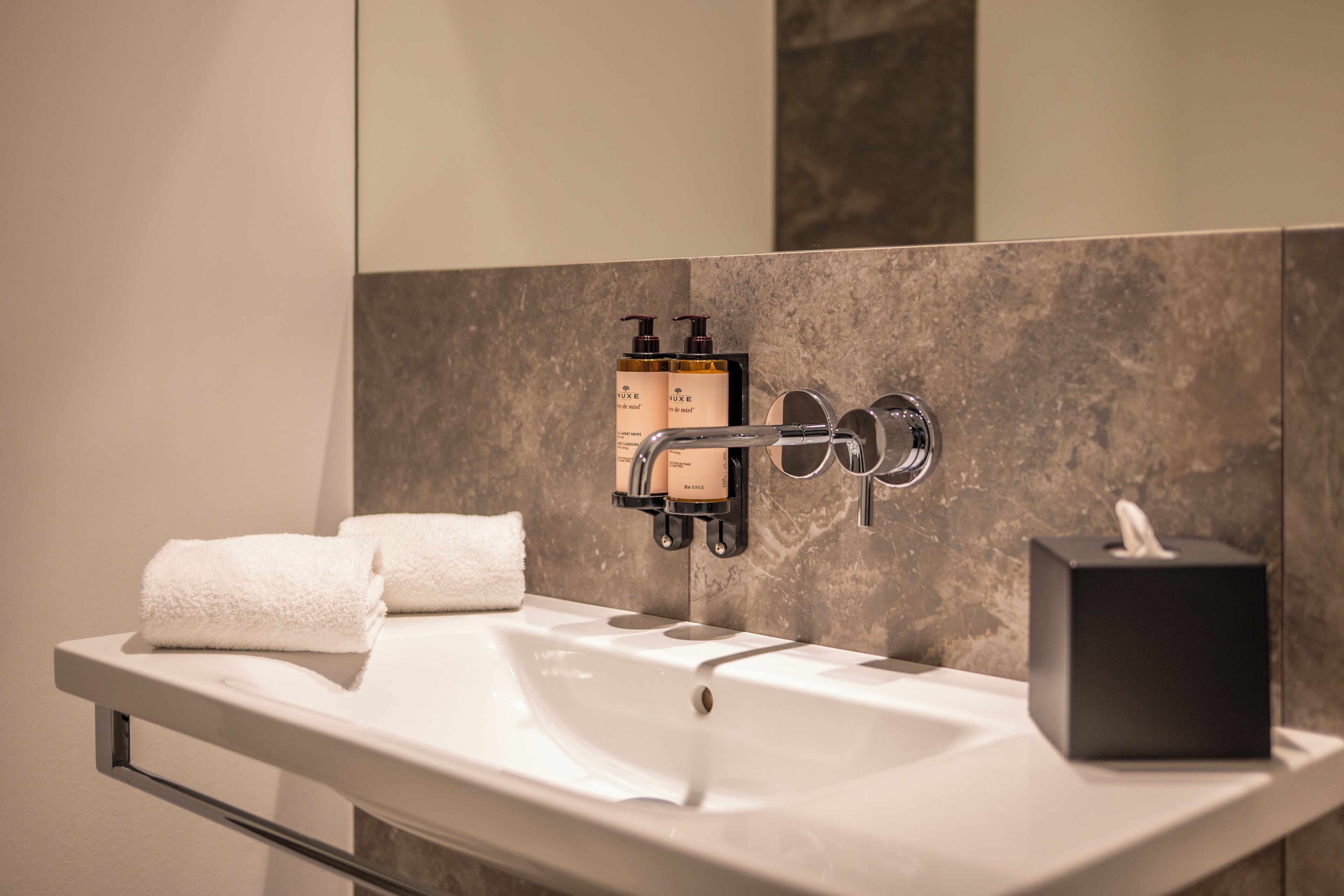 A modern bathroom with a white sink, two soap dispensers, a towel, and a tissue box.