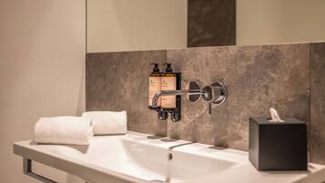 A modern bathroom with a white sink, two soap dispensers, a towel, and a tissue box.