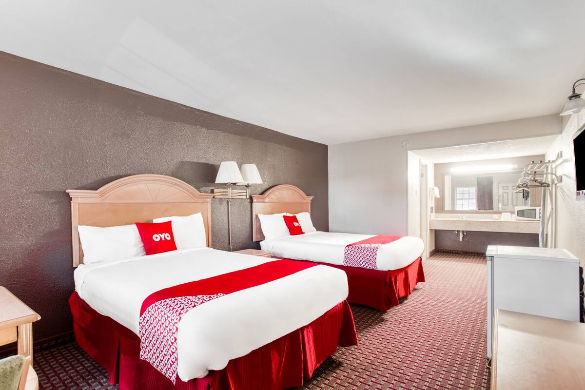 A hotel room with two beds, each with red and white bedding, a wooden headboard, a small table, and a chair.