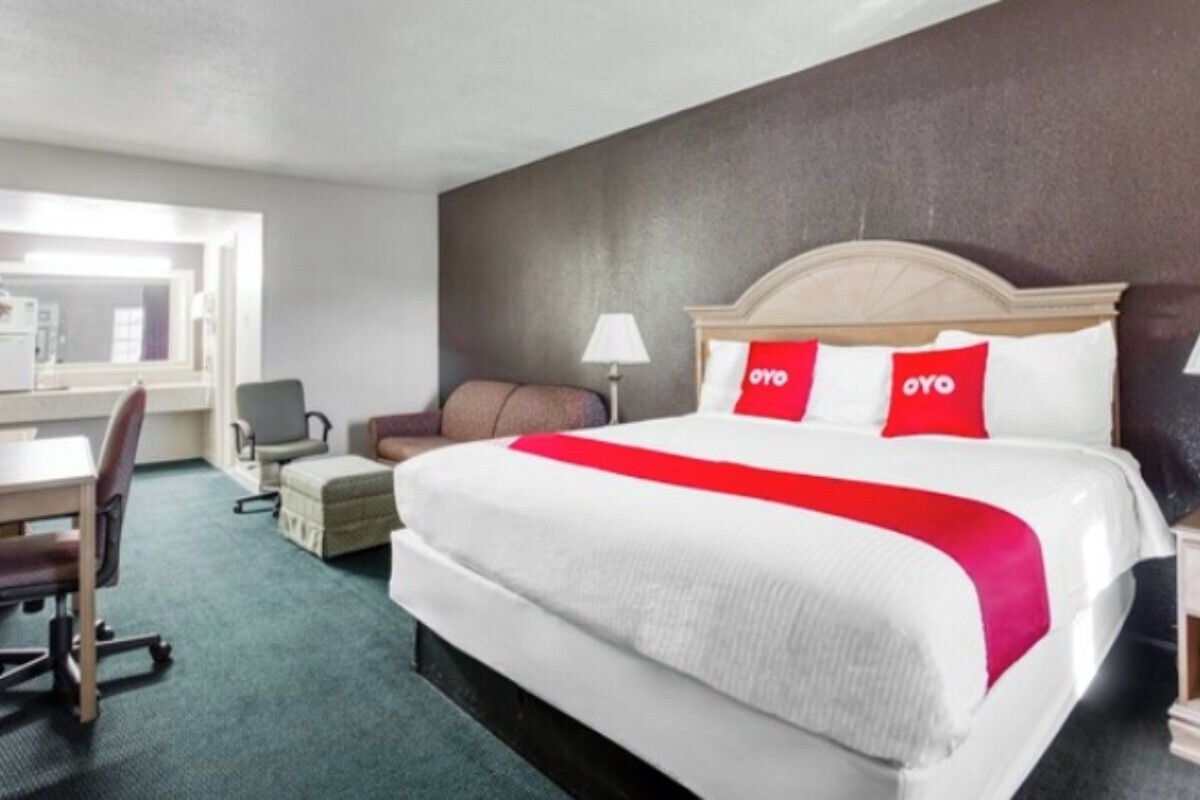 A hotel room with a bed, desk, chair, and a view of the kitchen area.
