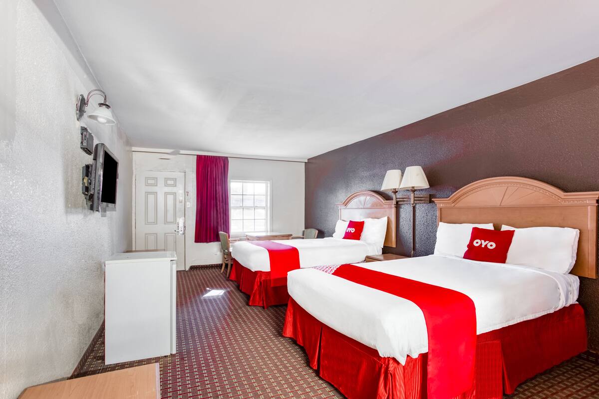 A hotel room with two beds, a desk, a refrigerator, and a window with curtains.