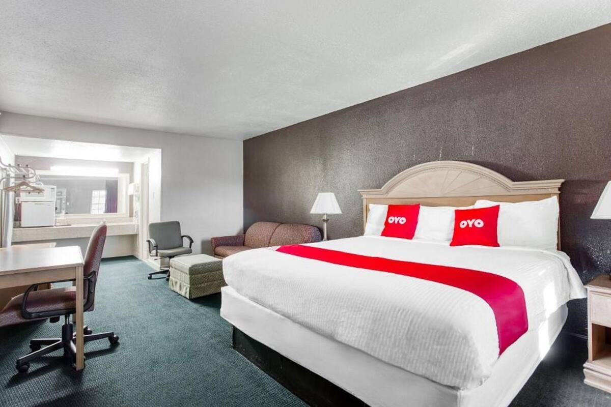 A hotel room with a bed, a desk, a chair, a lamp, and a small table.
