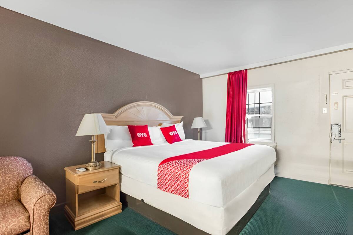 A hotel room with a bed, nightstand, lamp, and a chair.