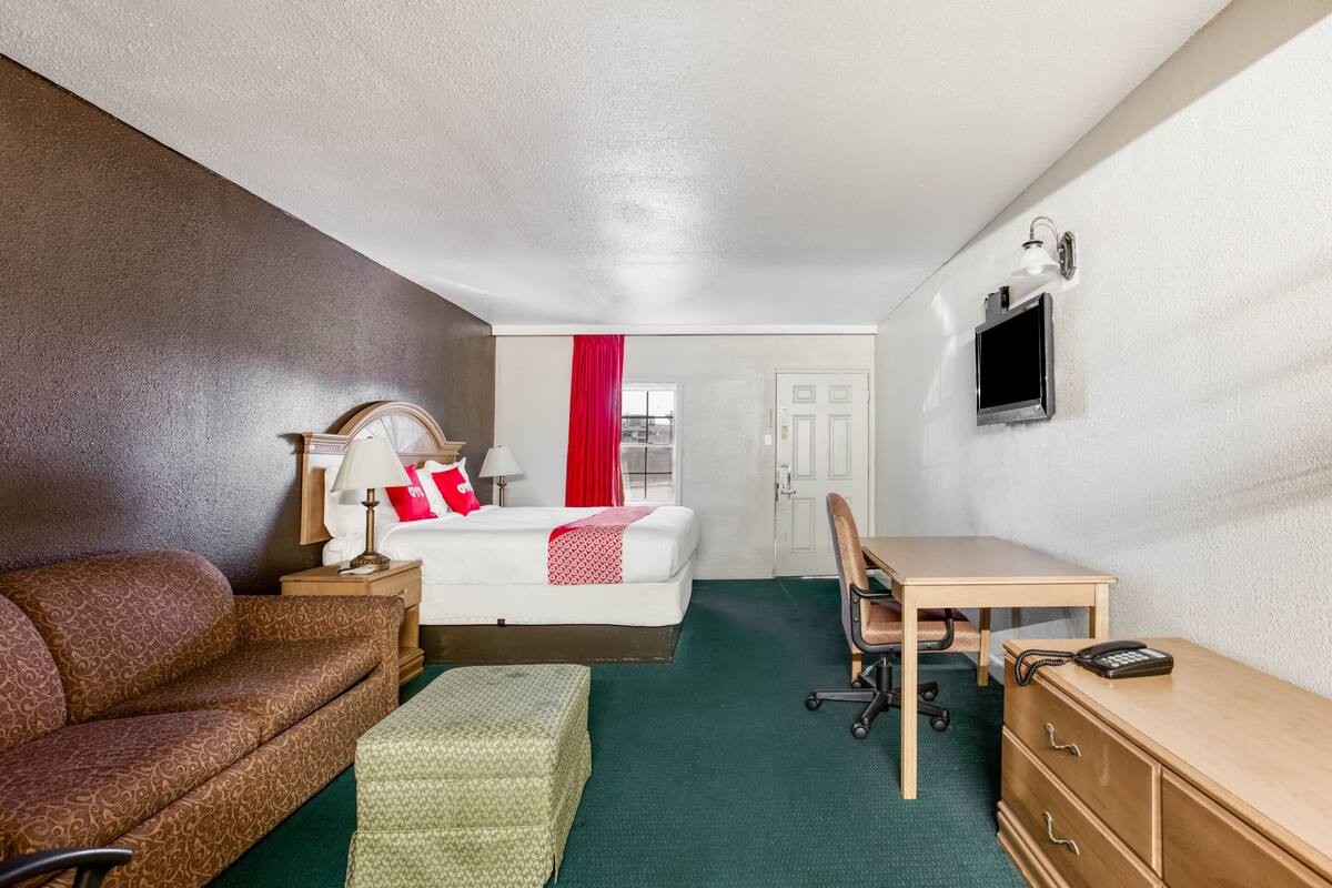 A hotel room with a bed, a desk, a chair, a sofa, and a TV.