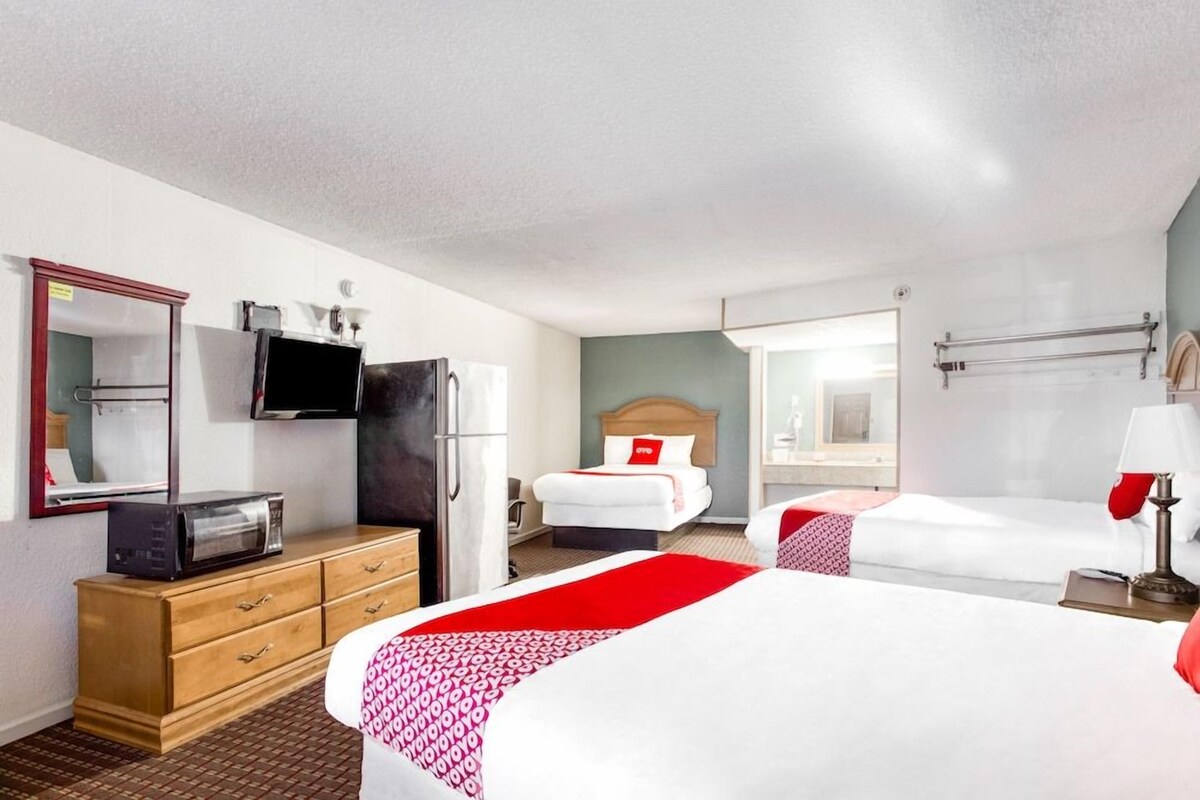 A hotel room with two beds, a television, a refrigerator, a wooden dresser, and a mirror.
