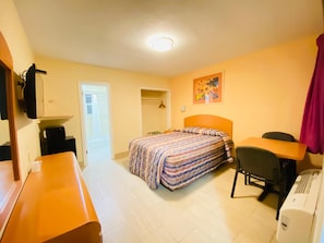 A hotel room with a bed, a desk, a chair, a heater, a wardrobe, and a door leading to a balcony. - A1A Super Inn (Ormond Beach)
