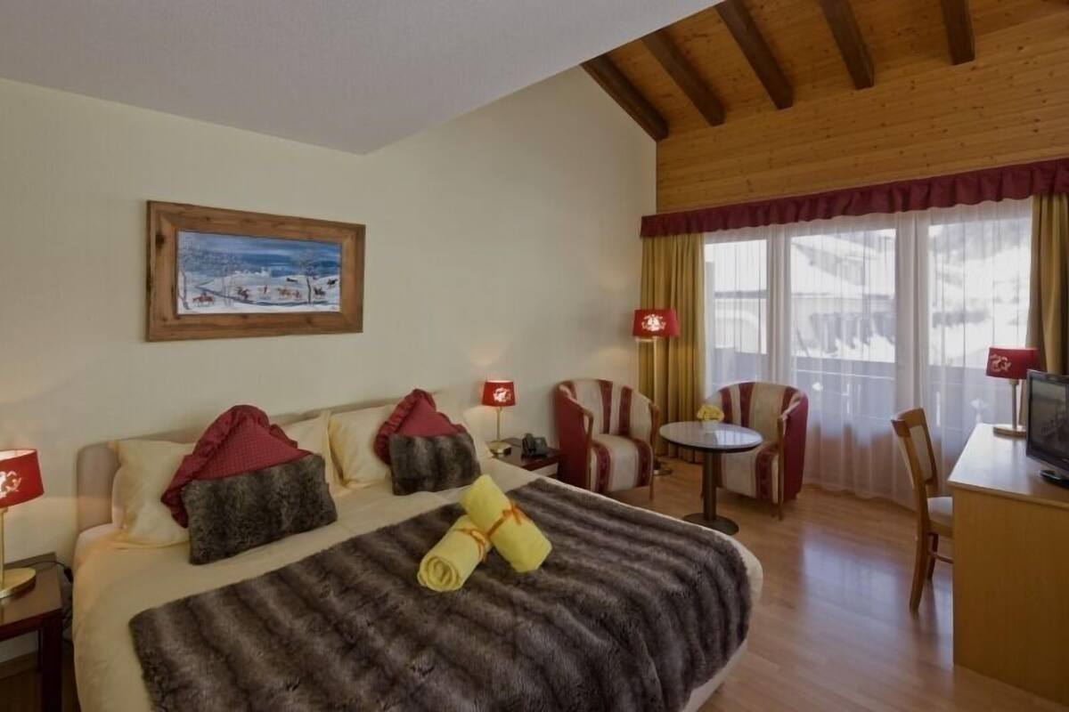 A hotel room with a bed, a desk, a chair, a TV, and a painting on the wall.
