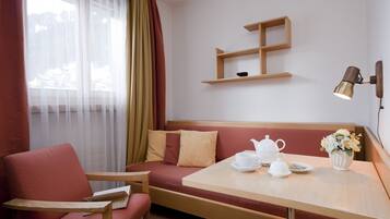 Une chambre d’hôtel accueillante, avec un banc en bois, une petite table sur laquelle se trouvent une théière et des tasses, un vase rempli de fleurs et une étagère fixée au mur.