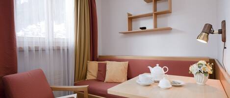 A cozy hotel room with a wooden bench, a small table with a teapot and cups, a vase with flowers, and a wall-mounted shelf.