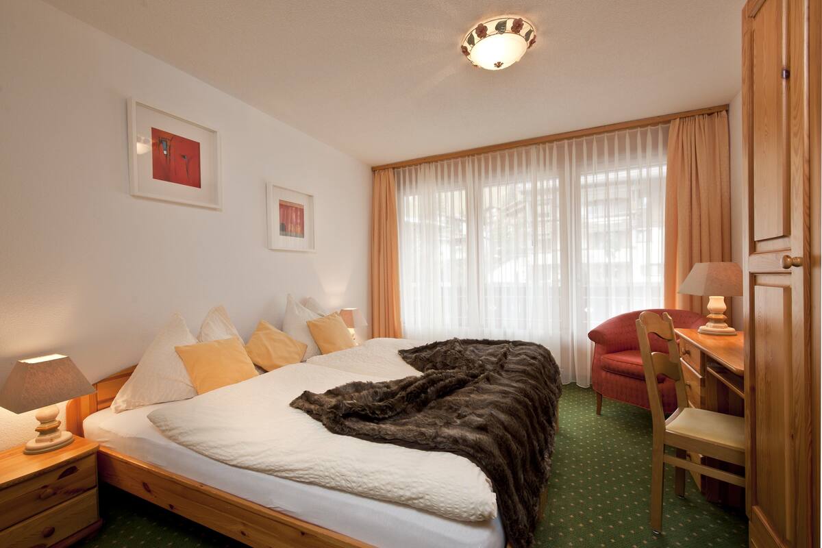 A neatly arranged bedroom with a bed, bedside tables, a chair, and a desk.