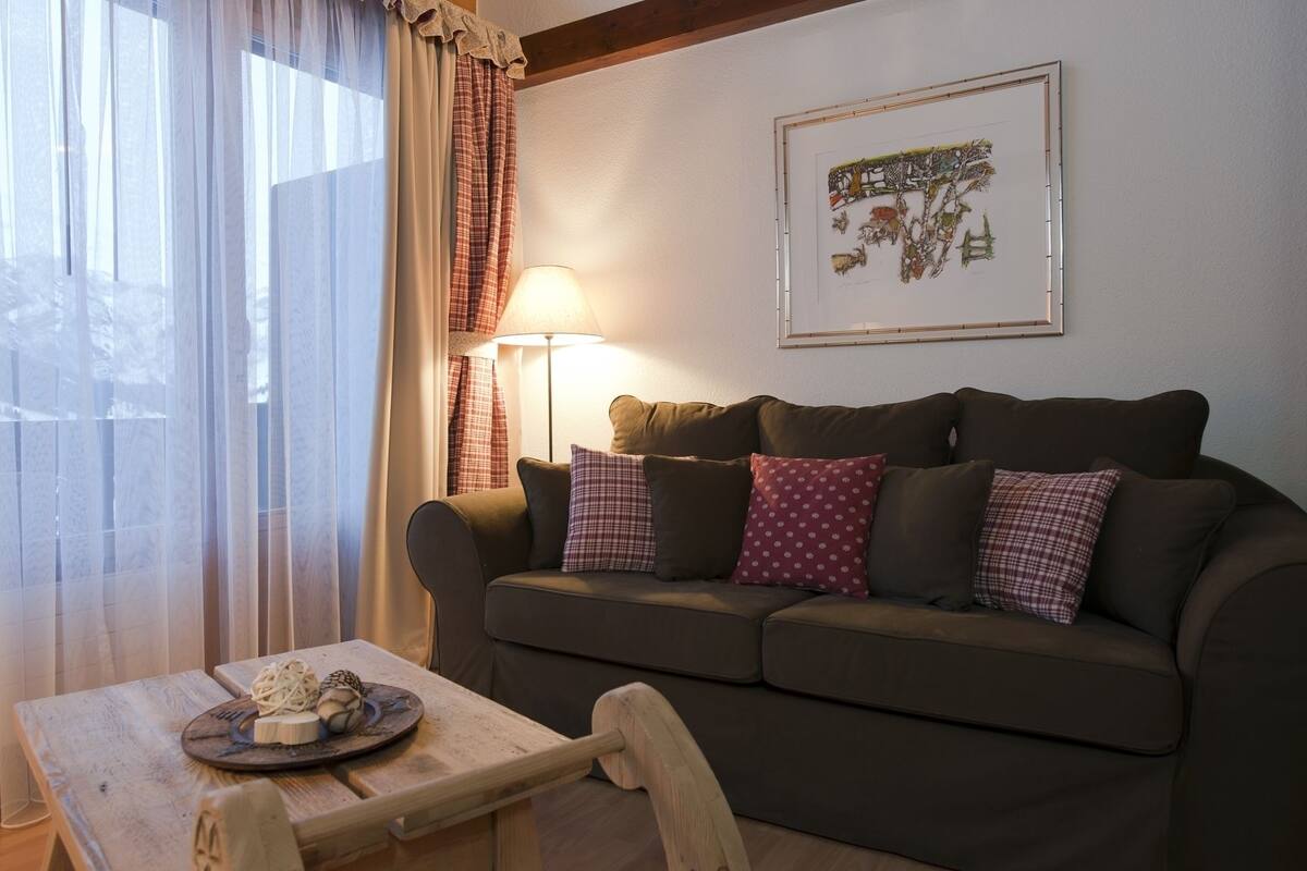 A cozy living room with a brown sofa, a wooden table with a plate of food, a lamp, and a framed picture on the wall.