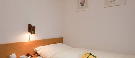 Habitación de hotel con cabecera de madera, mesita de noche con juego de té, toalla enrollada y dos cuadros de flores en la pared.