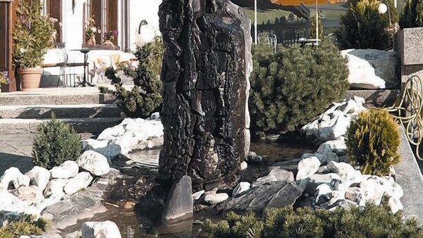 Un edificio con balcones adornados con flores, una estatua en primer plano y un paisaje montañoso de fondo.