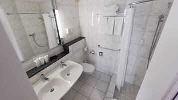 Un baño moderno con lavamanos doble, inodoro, zona de ducha y un espejo grande.