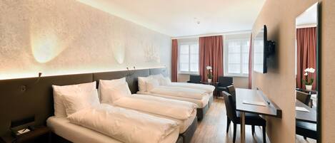 A hotel room with three beds, a desk, and a chair.