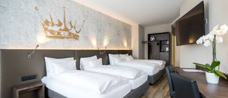 Habitación de hotel con una cama grande, un escritorio, una silla, un televisor y una pared decorada con un diseño de corona.