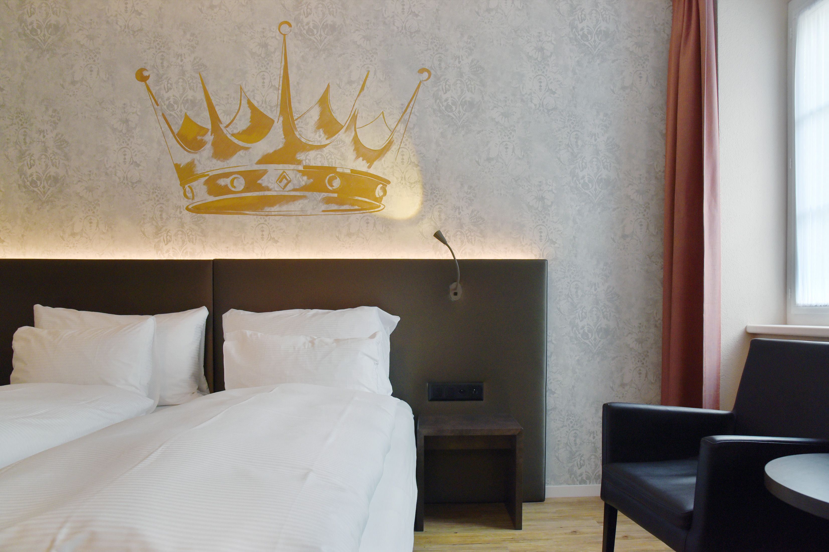 Ein Hotelzimmer mit einem großen Bett, einem Nachttisch, einem Sessel und einer Wandkrone.