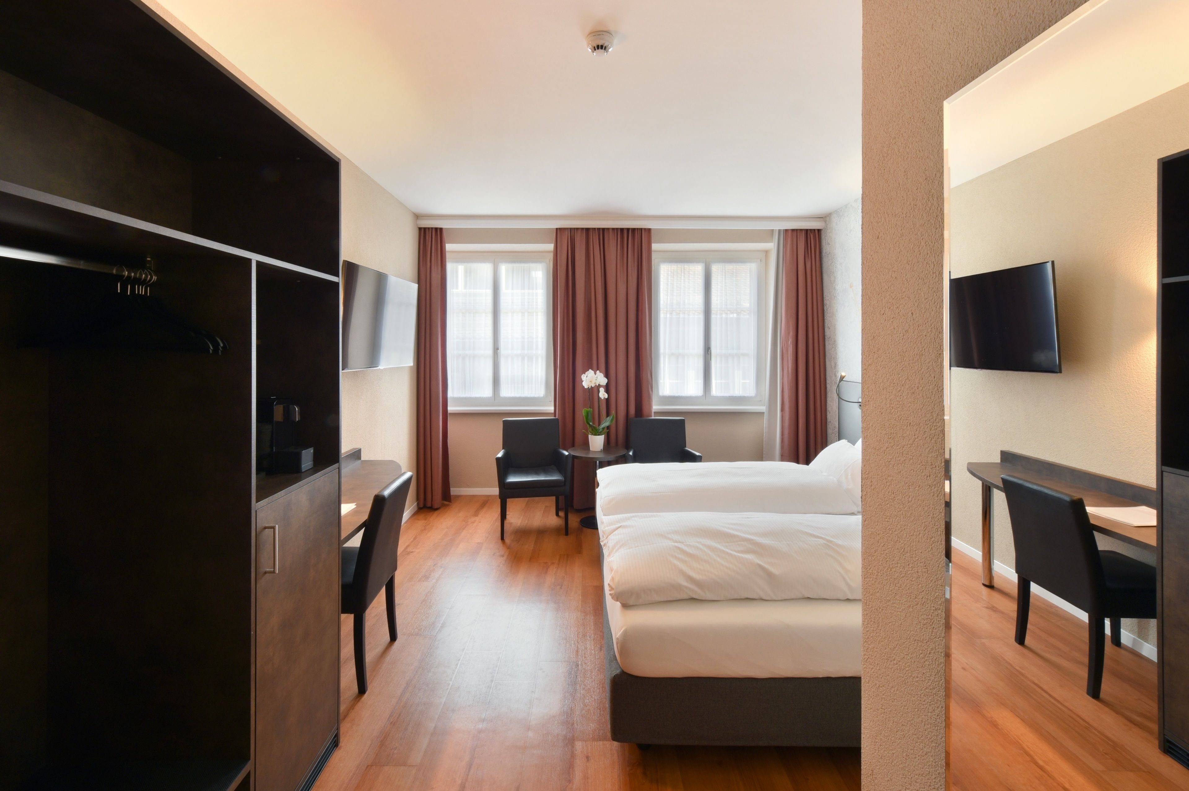 A hotel room with a bed, a desk, a chair, a TV, and a window with curtains.