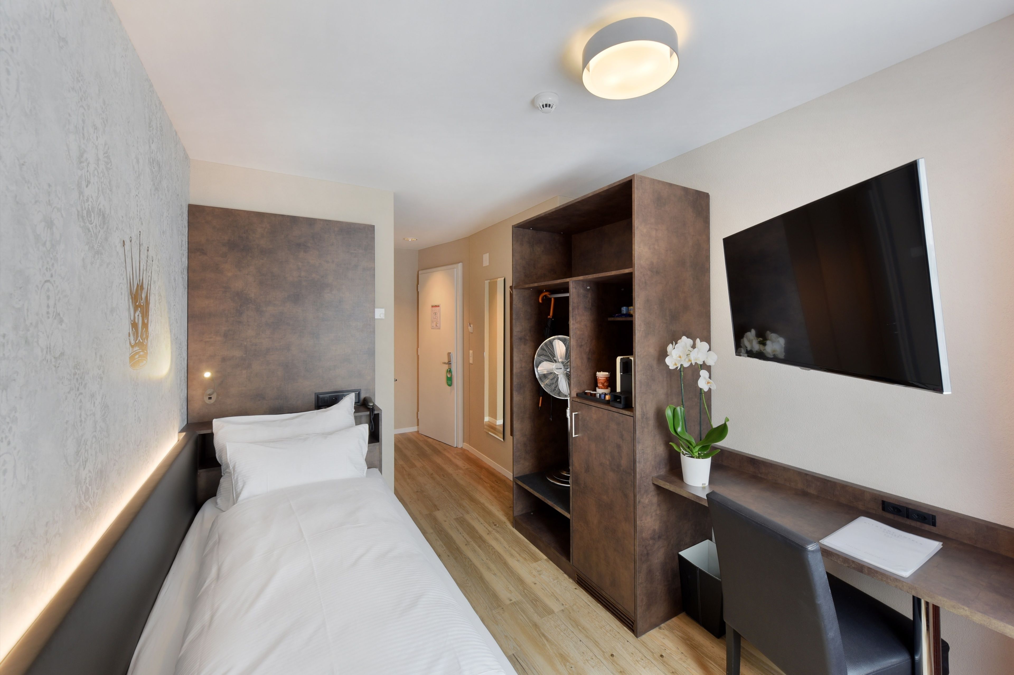 A modern hotel room with a bed, a desk, a wardrobe, and a large mirror.