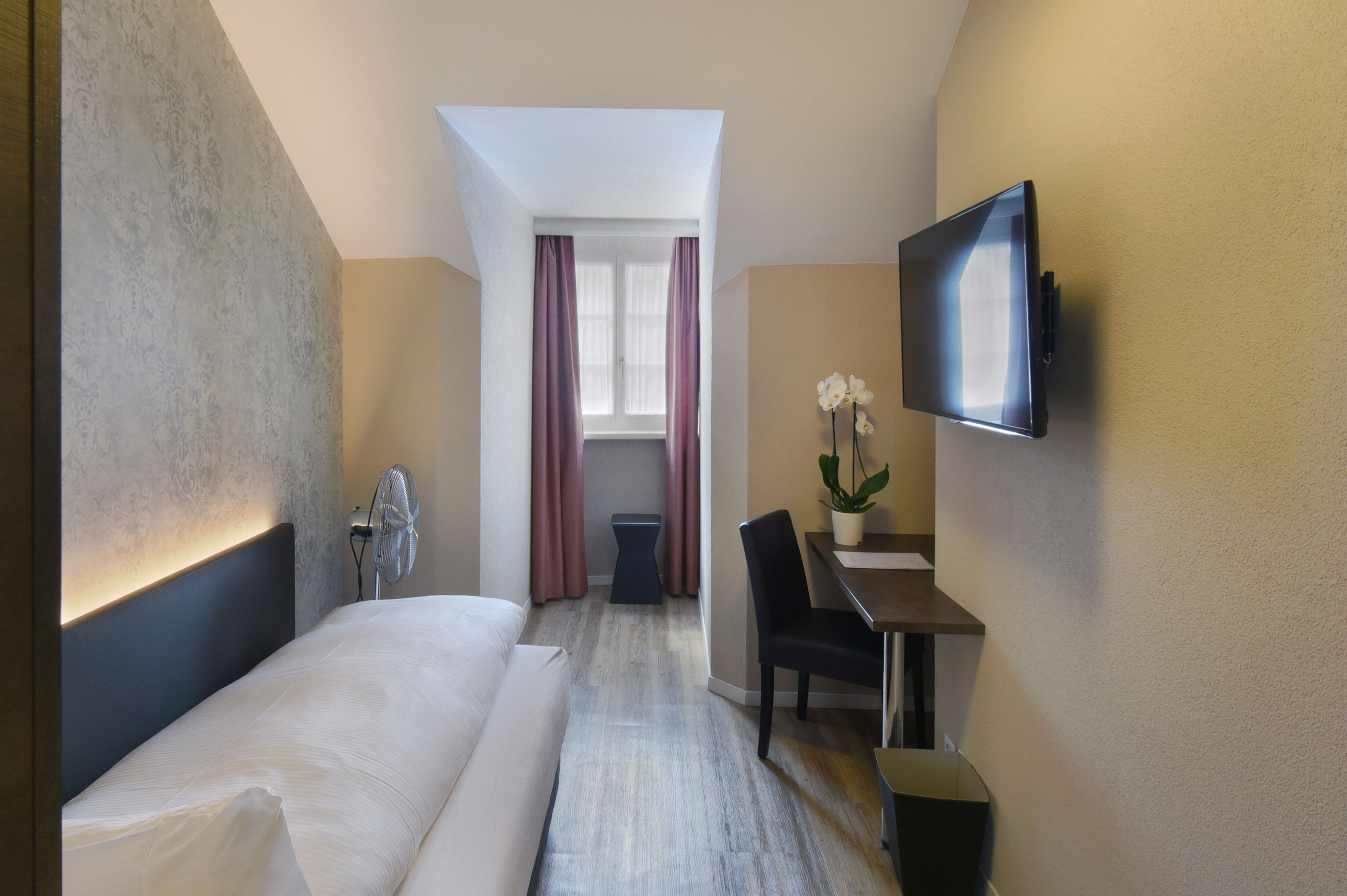 A hotel room with a bed, a desk, a chair, a TV, and a window with curtains.