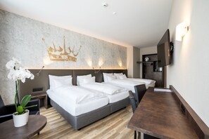 A hotel room with two beds, a wooden desk, a potted plant, and a wall-mounted TV. - Altstadt Hotel Krone Luzern (Lucerne)