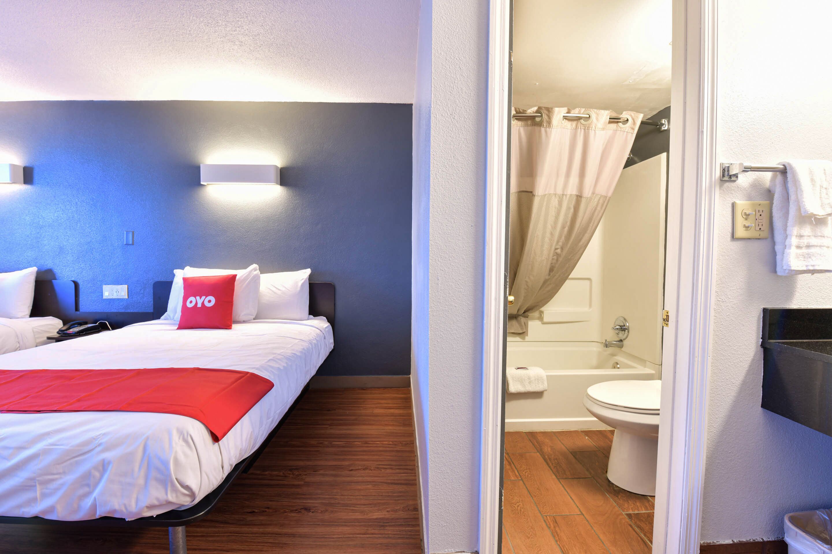 A hotel room with a bed, a red throw blanket, and a white pillow with "OYO" branding.