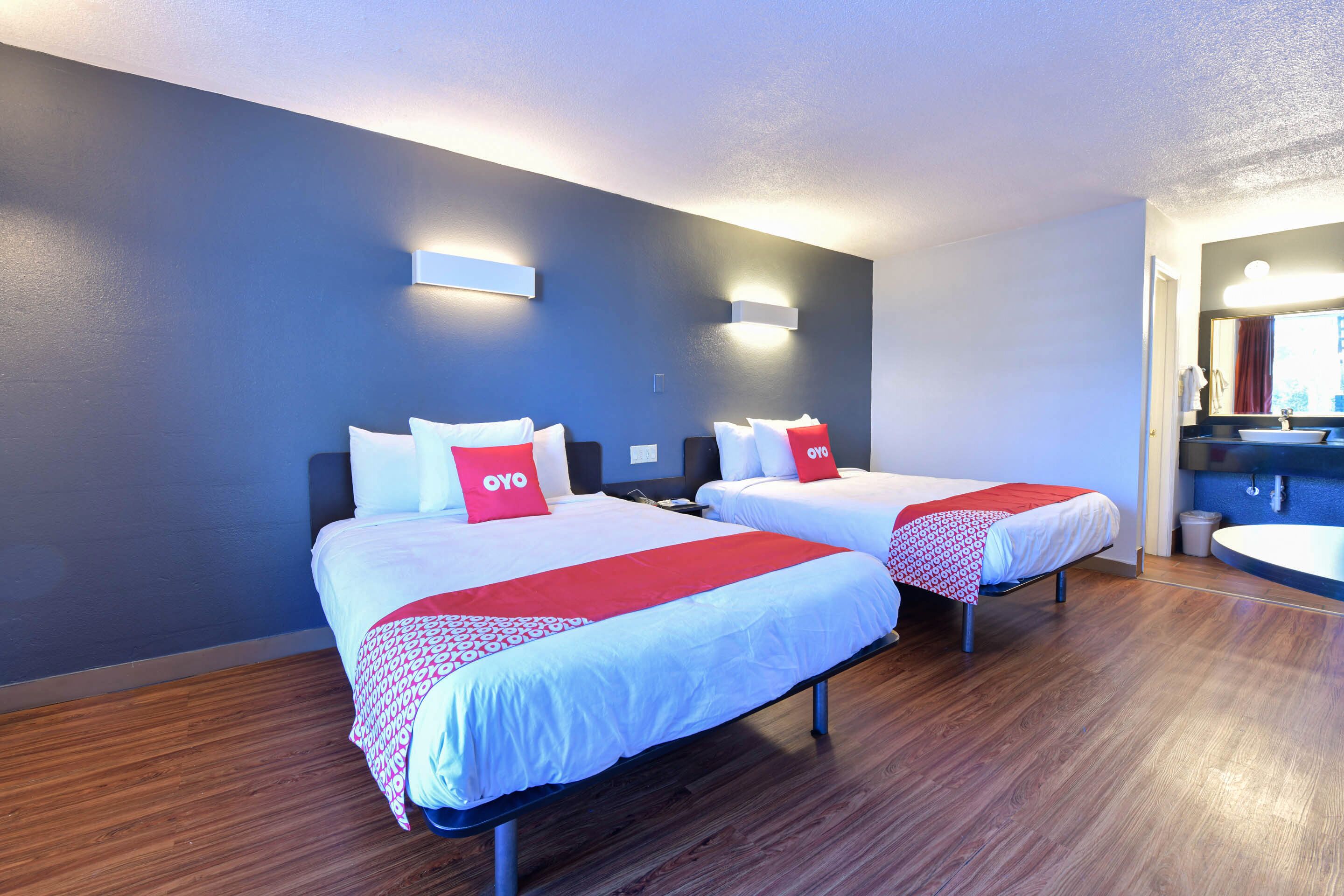 Ein Hotelzimmer mit zwei Betten, Holzboden und einem Badezimmer mit Waschbecken und Spiegel.