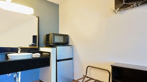Baño compacto con lavamanos, espejo y un microondas sobre un mini refrigerador.