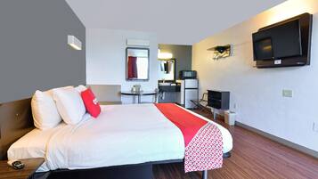 A hotel room with a bed, a desk, a chair, a TV, and a mirror.