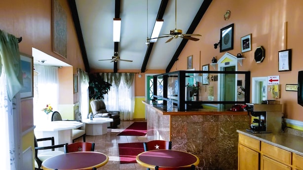 Eine Hotelhalle mit Empfangstresen, Sitzgelegenheiten mit Tischen und Stühlen, einer großen Pflanze und einem Deckenventilator.