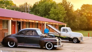 Ein Oldtimer und ein Lkw parken vor einem Gebäude mit rotem Dach.