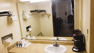 A hotel bathroom with a sink, mirror, towel rack, and a coffee maker.