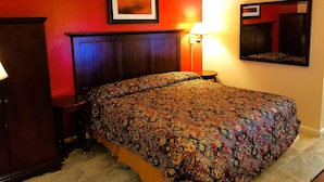 Ein Hotelzimmer mit einem großen Bett, einem hölzernen Kopfteil, einer roten Akzentwand, einem gerahmten Bild, einer Nachttischlampe und einem Spiegel.