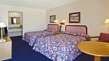 A hotel room with two beds, a desk, a chair, a round table, a mirror with lights, and two wall-mounted lamps.