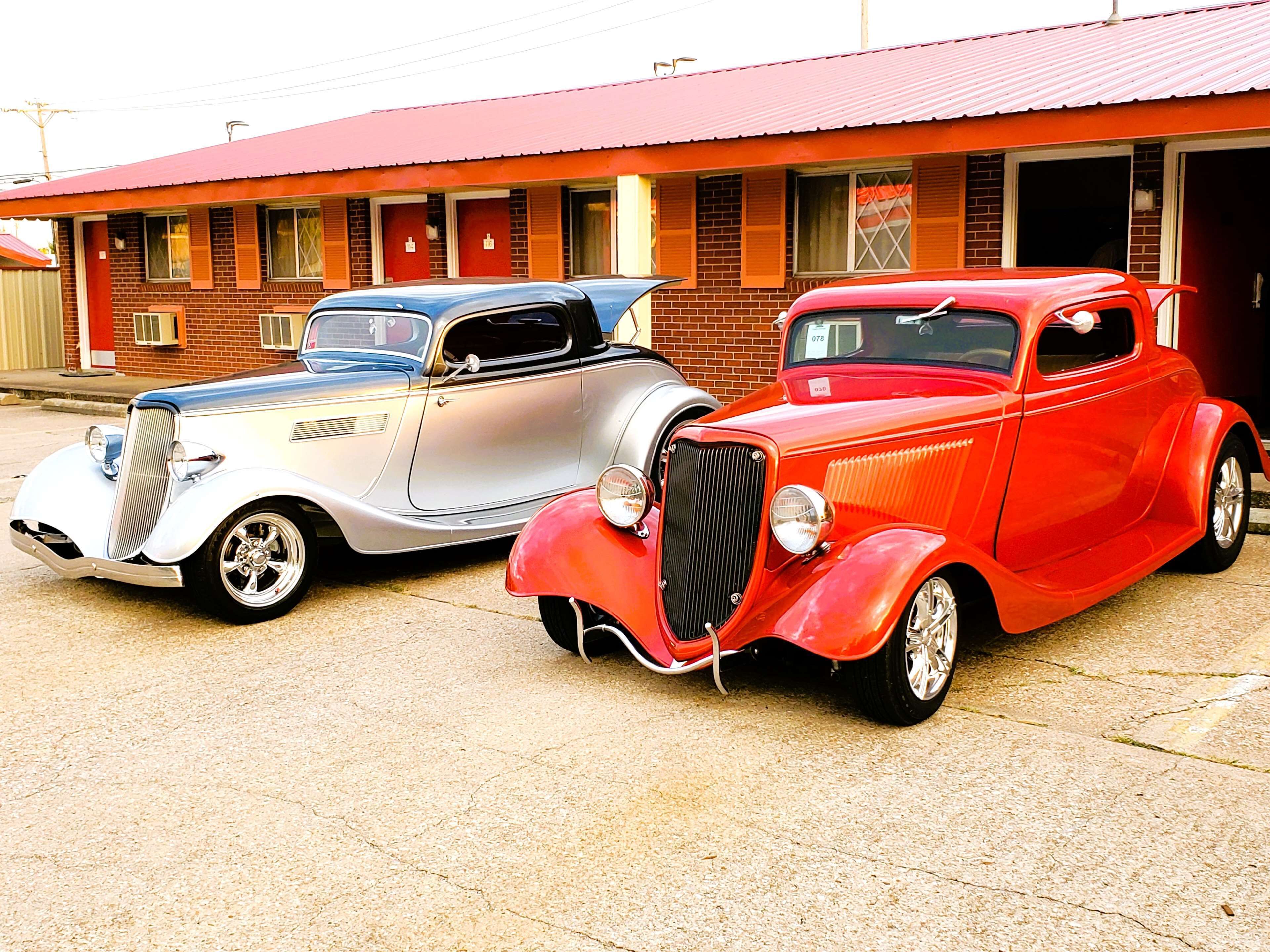 Two vintage cars parked in front of a building with a red roof and brick walls.