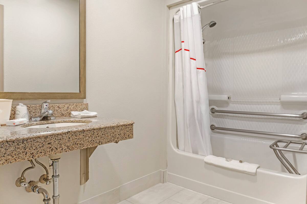 A bathroom with a granite countertop sink, a mirror, and a shower with a white curtain.