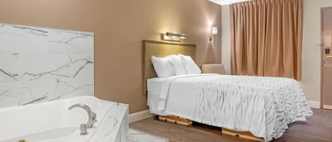 A hotel room with a marble bathroom, a bed with a white comforter, and a wooden floor.