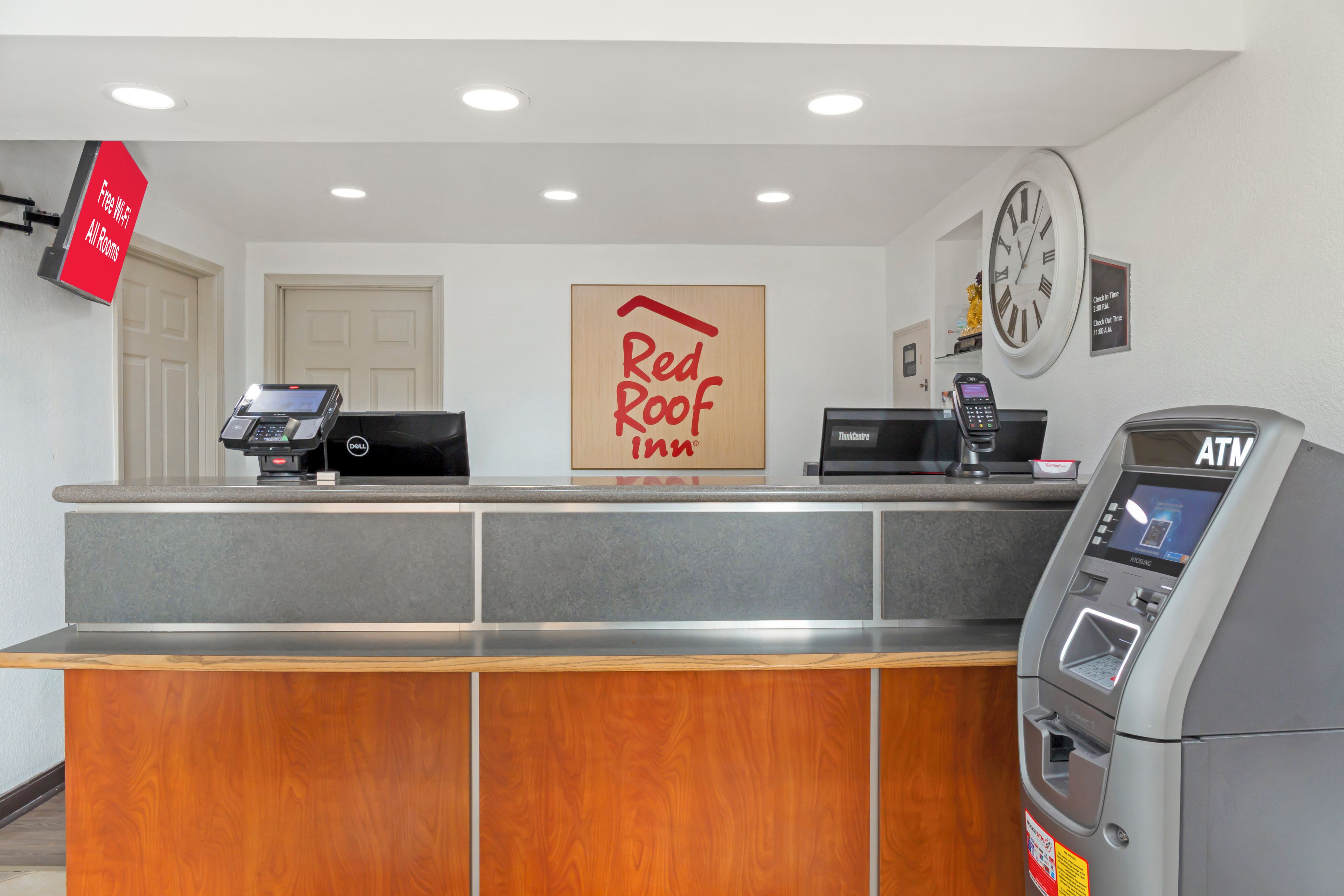 A hotel reception desk with a Red Roof Inn sign, a clock, and an ATM.