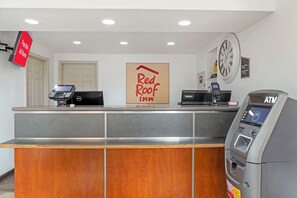 Un comptoir d’accueil d’hôtel avec une enseigne Red Roof Inn, une horloge et un distributeur automatique de billets.