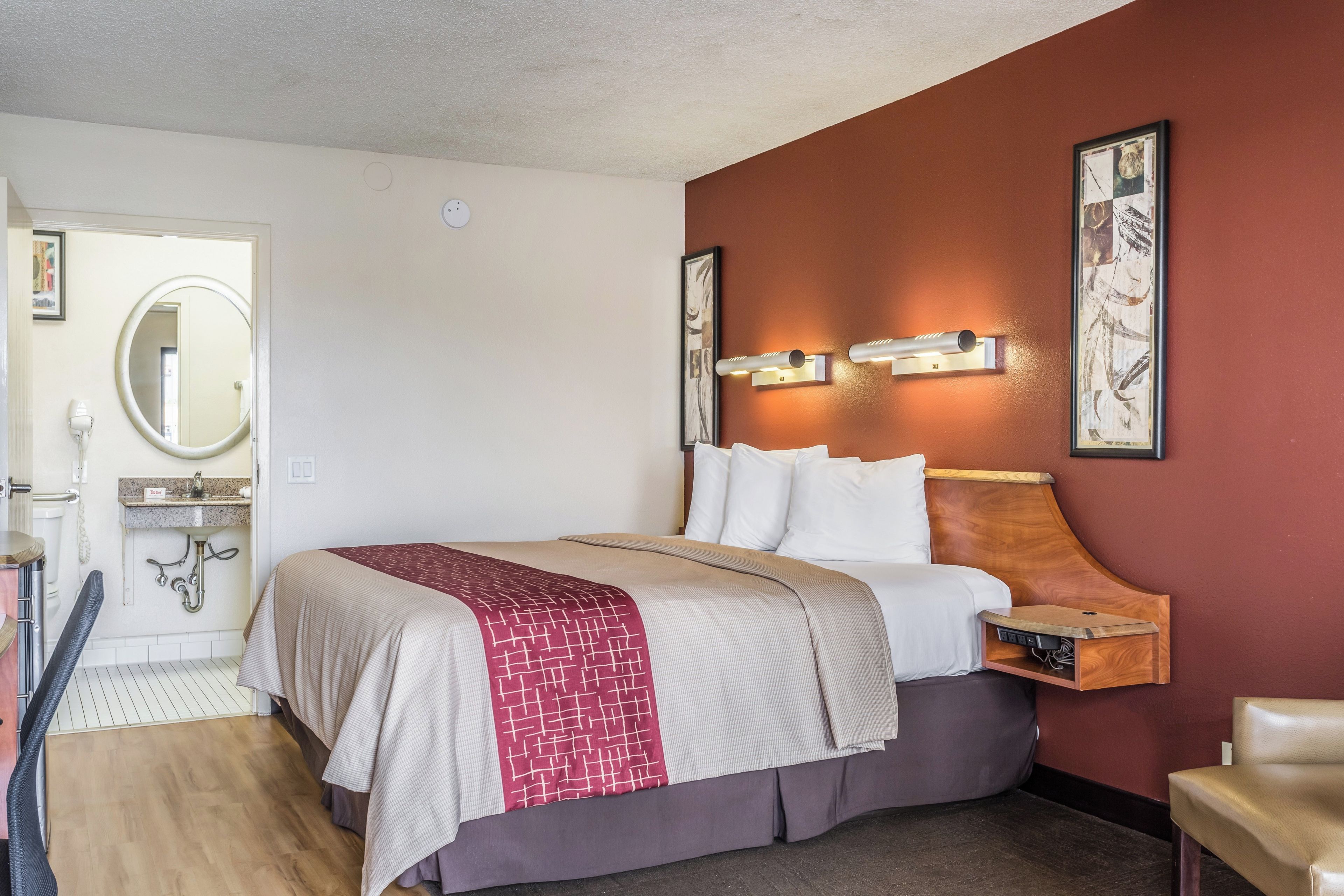 Une chambre d’hôtel comprenant un lit, une table de chevet, une lampe fixée au mur et un miroir.