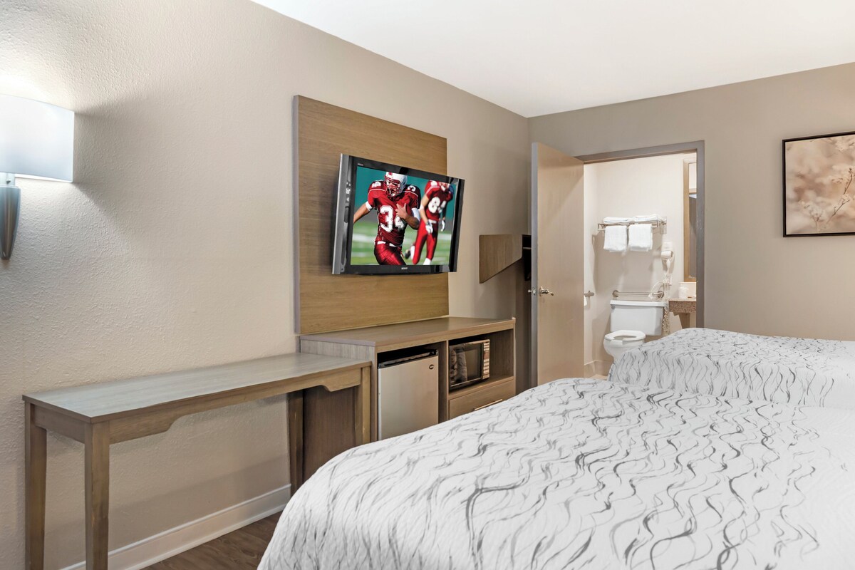 A hotel room with a bed, a TV mounted on the wall, a desk, and a bathroom visible through an open door.