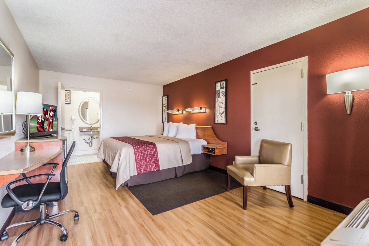A hotel room with a bed, a desk, a chair, a TV, and a door.