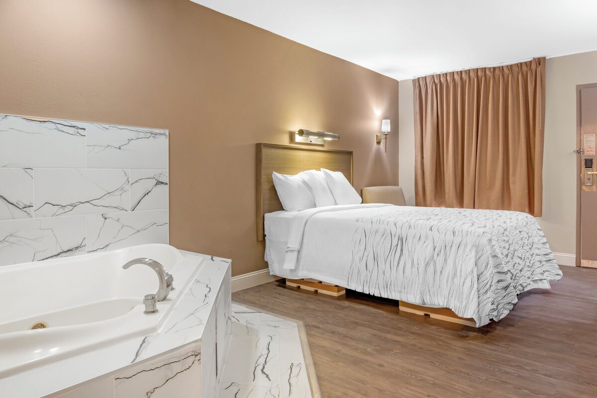 A hotel room with a marble bathroom, a bed with a white comforter, and a wooden floor.